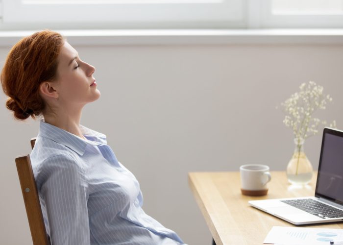 Side view female resting with closed eyes at work Side view young calm female sitting at office desk in workplace opposite computer with closed eyes daydreaming breathing fresh air. Finishing work satisfied businesswoman resting relaxing feels good